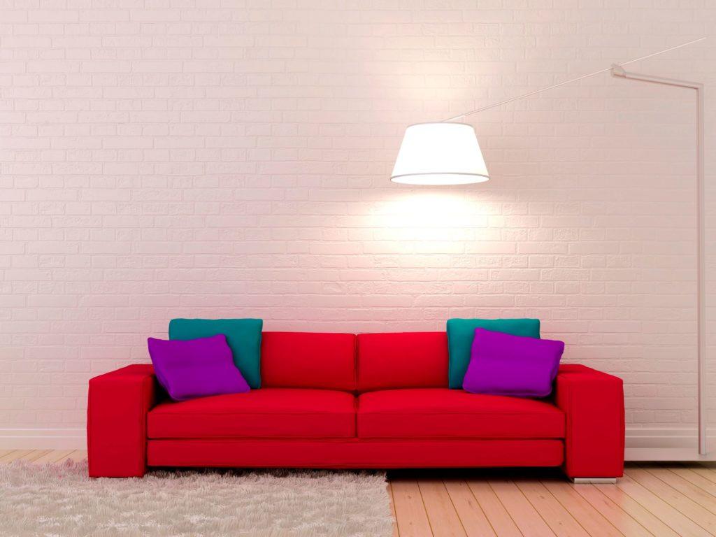 Яркий красный диван у светлой стены под кирпич